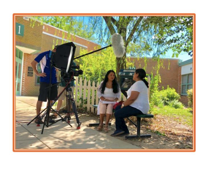 Two women talking outside on a bench with a camera crew recording them.