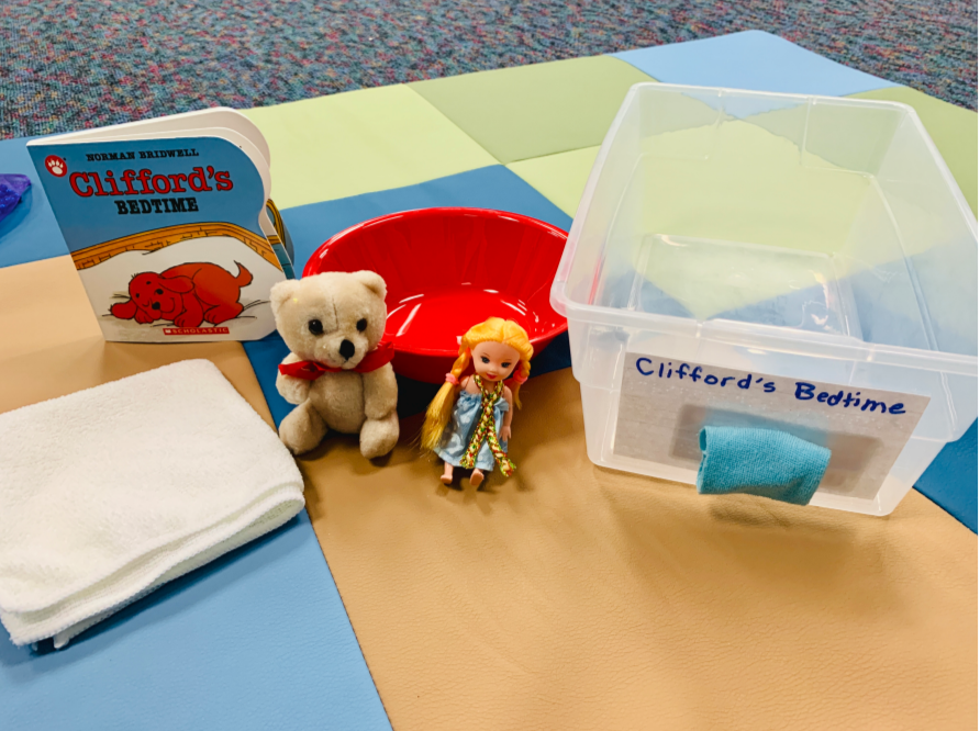 Clifford's Bedtime Book with a container labeled "Clifford's Bedtime" and a small blanket square under it. Objects include a small doll, bear, and bowl.