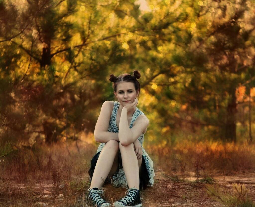 young adult sitting in the forest with a smile.