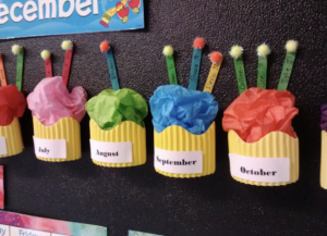 Birthday bulletin board hat has textured 3-D textured, paper cupcakes for each month and then popsicle stick as candles with students name on them.