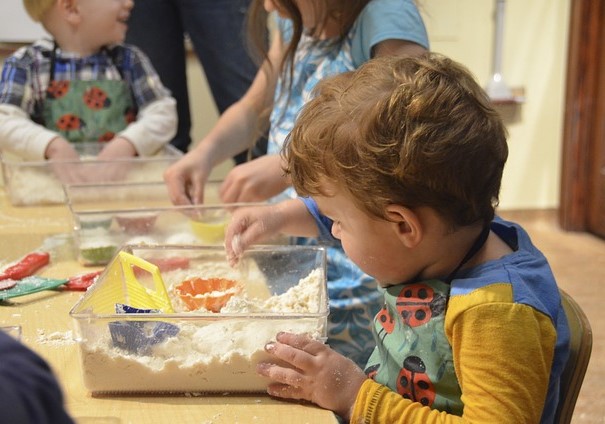 Young children at a table, each have a sand bin and are playing with toys in it