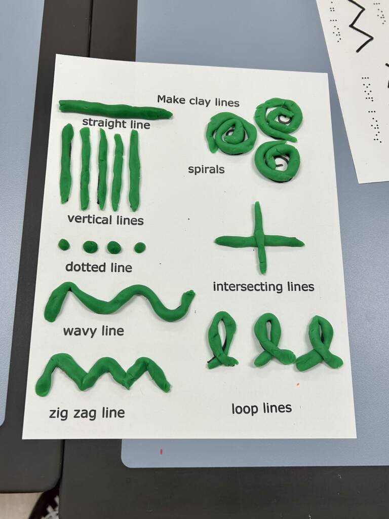 A piece of paper with various lines such as vertical, straight, and dotted is shown. Playdough formed to the same shape as those lines are put over the lines on the sheet of paper.