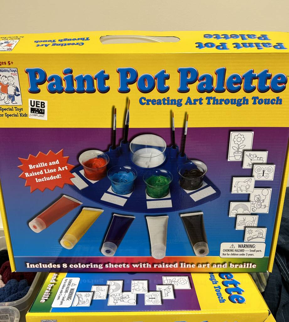 Photo of the Paint Pot Palette kit, which includes a paint tray, paint, brushes, cups, and various drawings.