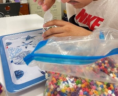 Student scooping beads and filling them into a bottle.