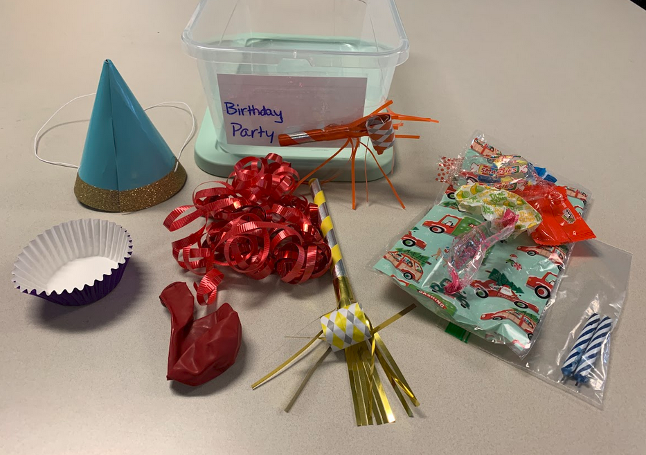 Birthday box container with a paper hat, ribbon, candles, cupcake wrappers, blow horn, and balloon.