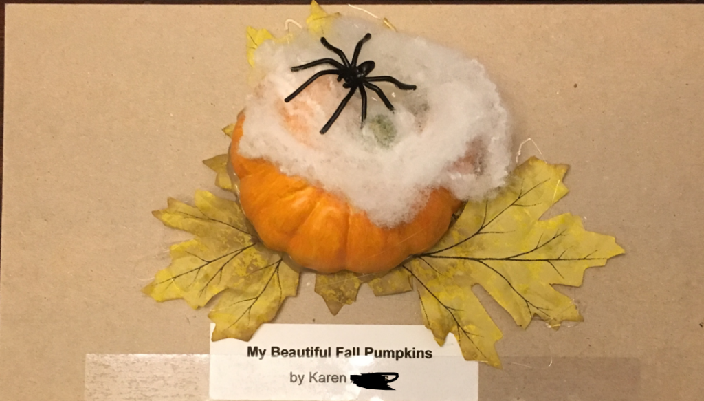 A small pumpkin with autumn leaves, fake spider webs, and a plastic spider arranged onto it