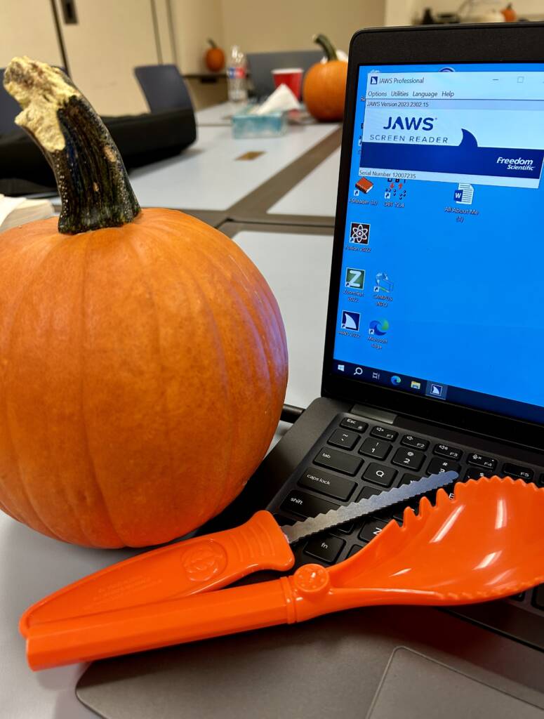 A pumpkin with a carver and a scoop next to a laptop computer with JAWS accessibility on it