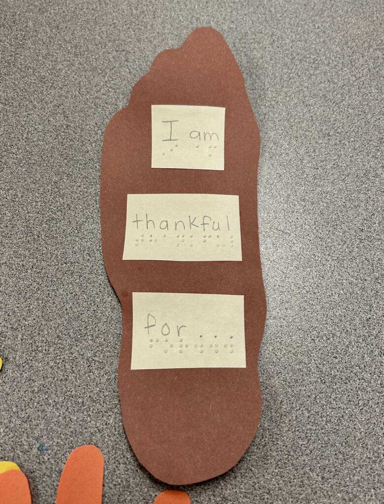 Paper cut out of a foot and on it says I am thankful for, in print and braille.