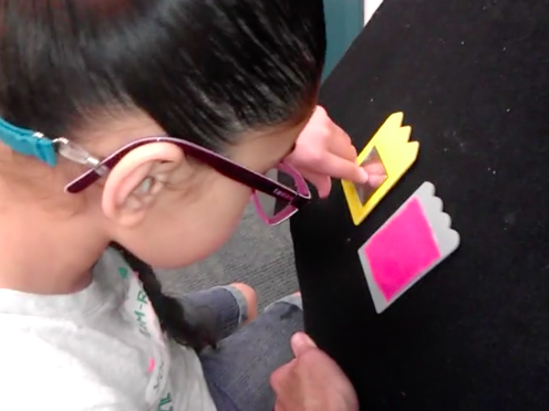 Girl wearing glasses points at tactile symbol on slant board with black background