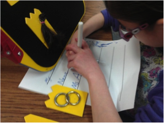 Student writing using blue marker with tactile symbols on raised black background at eye level