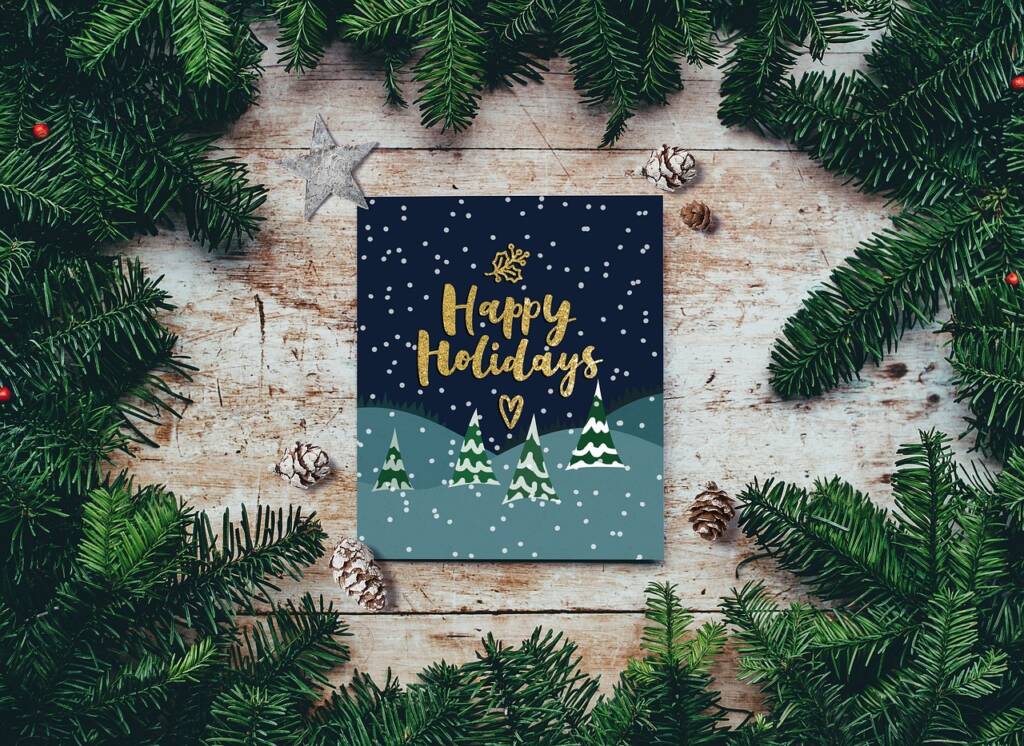 A card saying "Happy Holidays" on it surrounded by pine tree branches