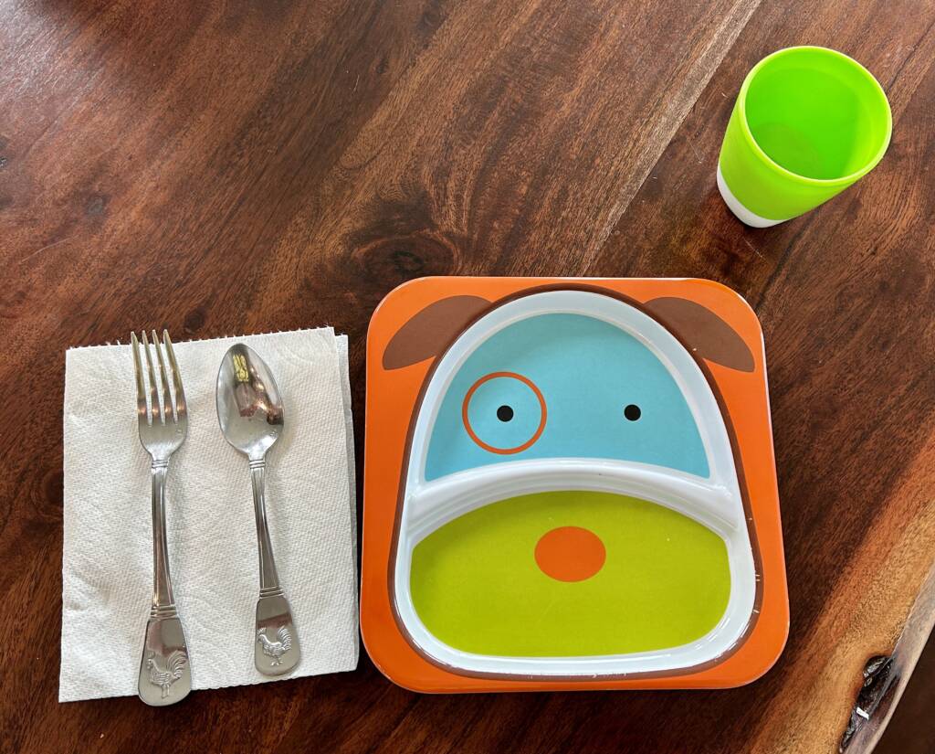Child's plate with a cup, fork, spoon, and napkin.