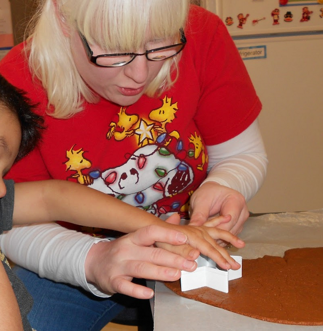 A woman helping a young boy press a star shaped cookie cutter into the flat piece of dough.