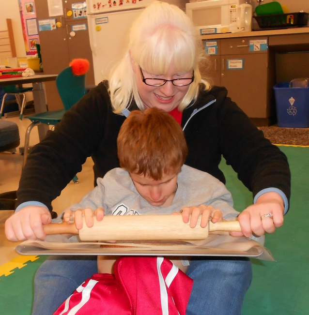 A woman helping a young boy roll out the dough using a rolling pin