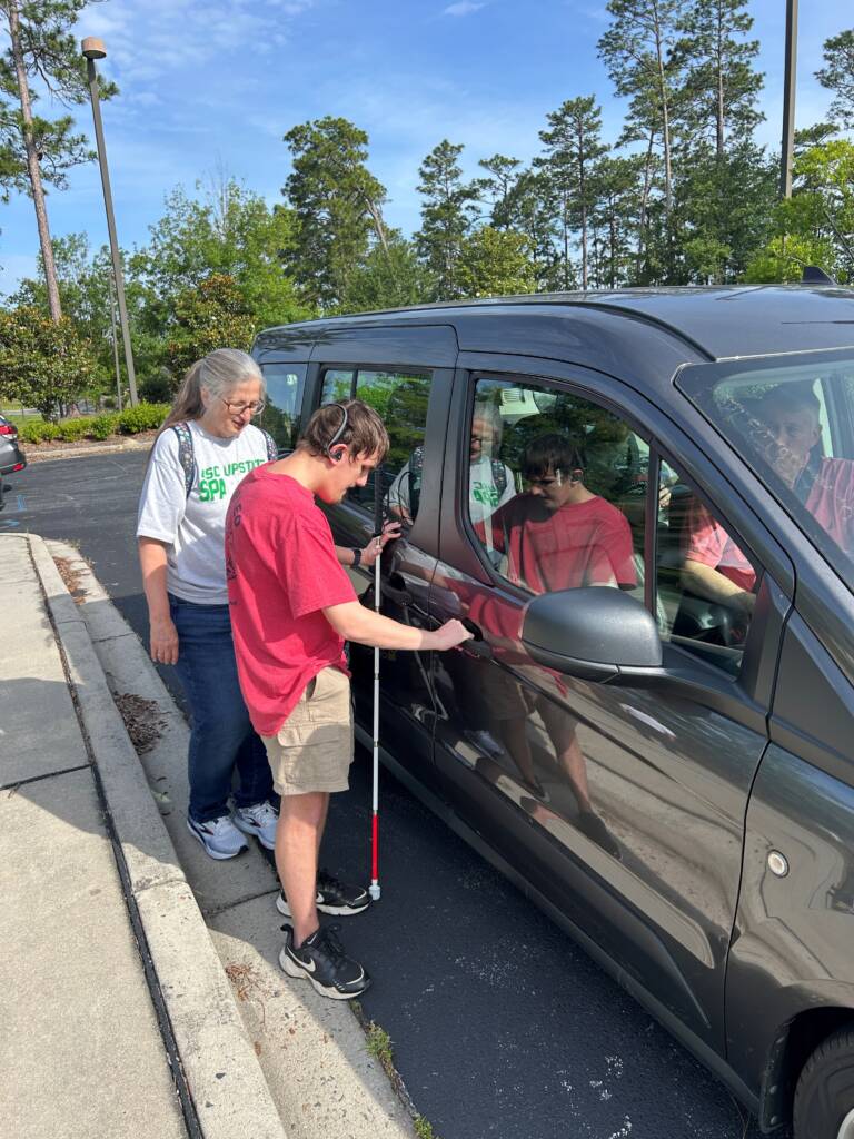 A male traveler is locating the front door of a vehicle as Dr. Herzberg observes.