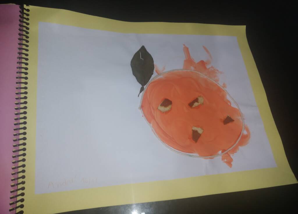 colored image of a sheet of paper containing a circular painting made with
Orange paint with a white string outline. There are pieces of orange peel glued to the painting and an
orange leaf glued to the outside of the string outline.