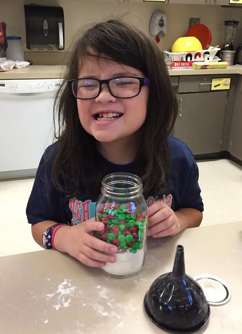 A student smiling while holding a mason jar filled with the cookie ingredients.
