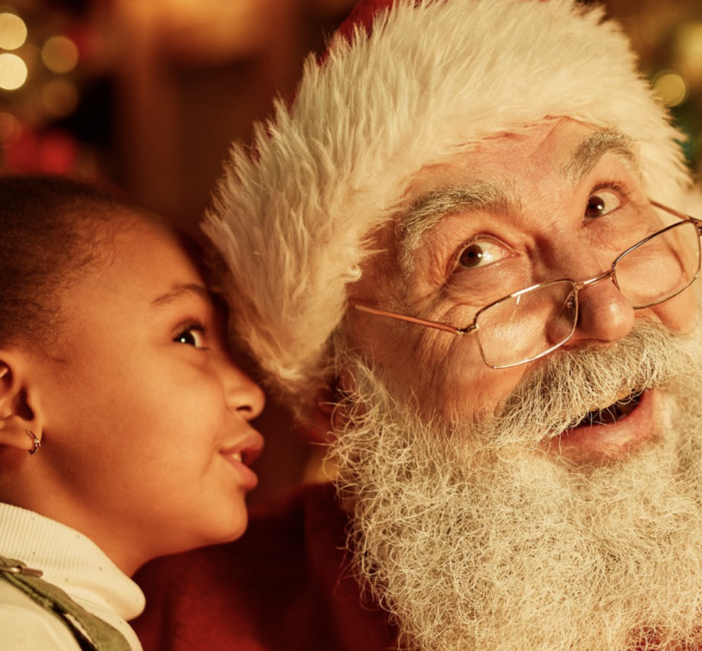 A little girl whispers into Santa's ear