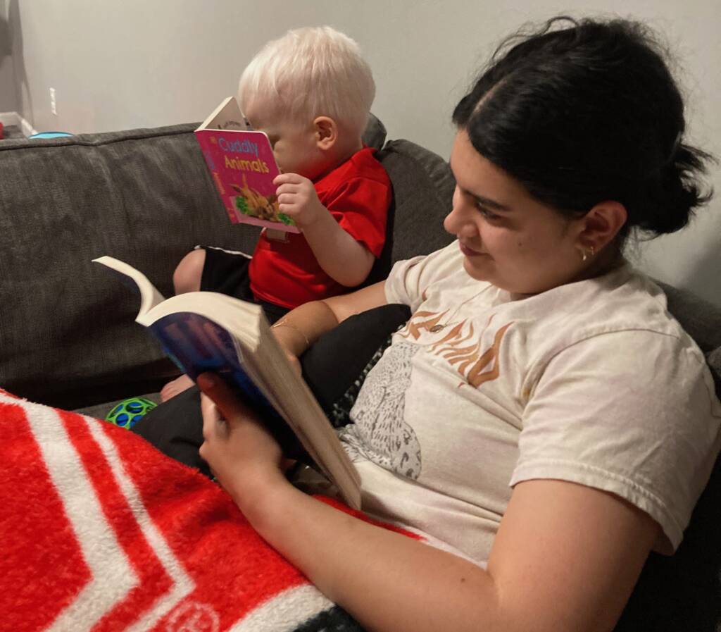 A toddler looks at a board book next to his mother.