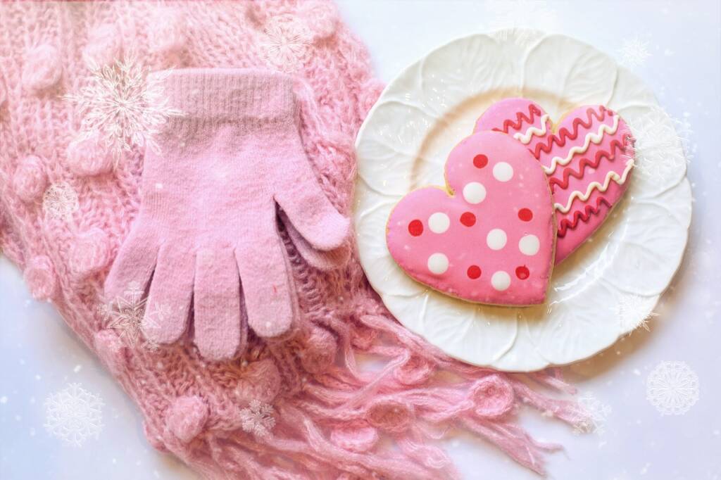 A pair of gloves and a scarf sitting next to a plate of heart shaped cookies