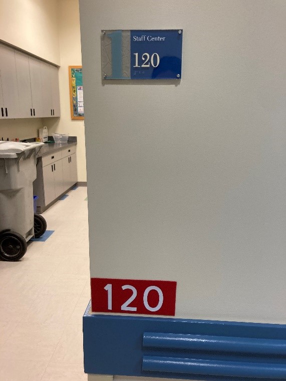A wall that has the original room number sign that says "staff center, 120" and an additional room number sign reading "120" placed below that