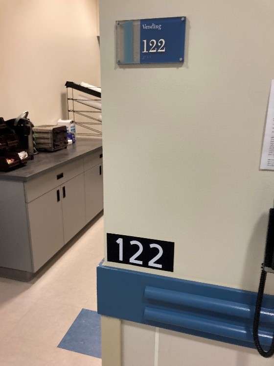 A wall that has the original room number sign that says "vending 122" and an additional room number sign reading "122" placed below that