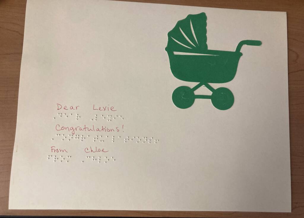 A greeting card with a picture of a baby stroller on it and the words "Dear Lexie, Congratulations! From Chloe" written in both print and braille. 