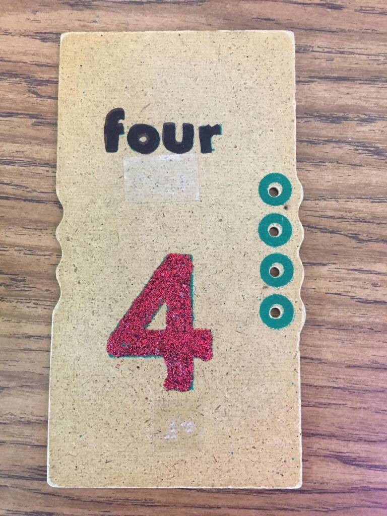 Adapted card with the number four in print and braille and four green circles around punched out holes