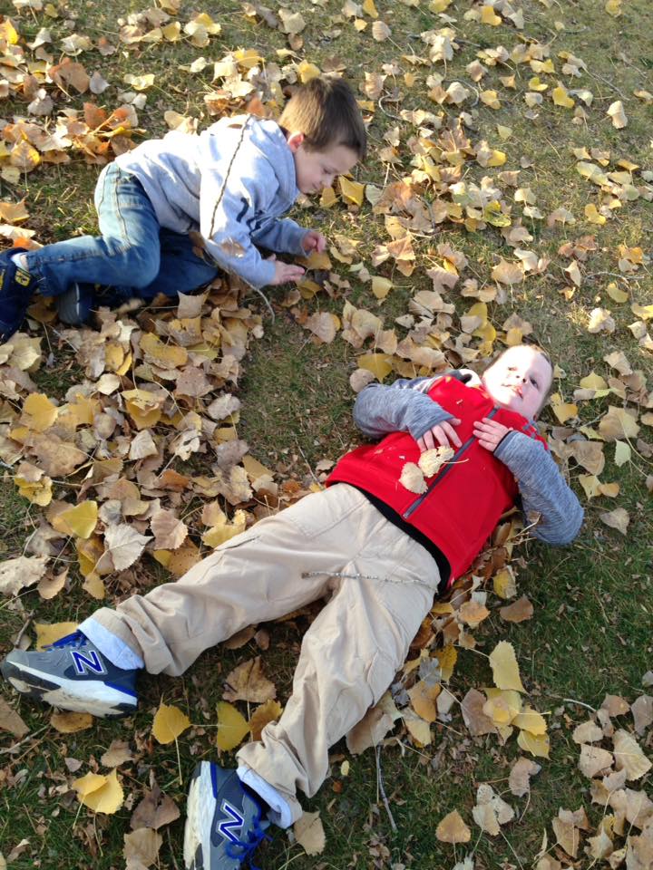 two boys lying on the ground with fall leaves