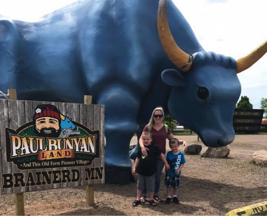 A mother stands with her two young sons in front of a large statue of a blue ox at Paul Bunyan Land