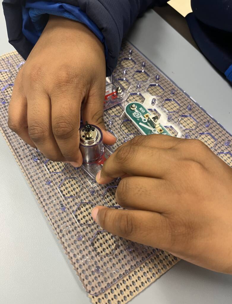 A student's hands assembling parts of the snap circuits Jr access kit
