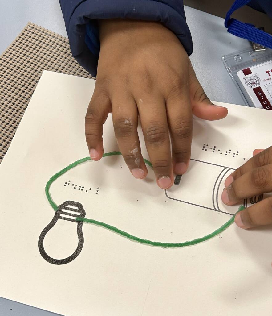 A student using Wikki Stix to create a circuit on the tactile graphic