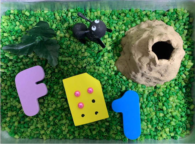 container with small green pasta and in it is an ant, ant hill, the letter f in braille.