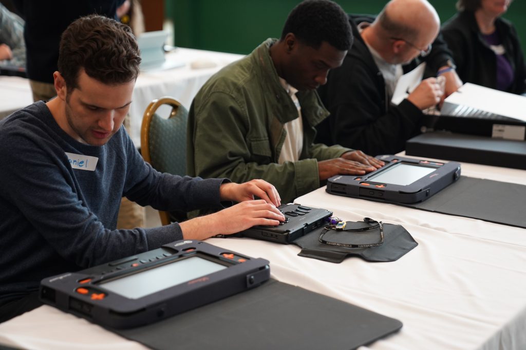 Three adults sitting at a table using the Monarch devices.