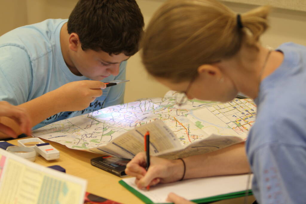 A student uses a hand-held magnifier while another writes notes on a pad pf paper