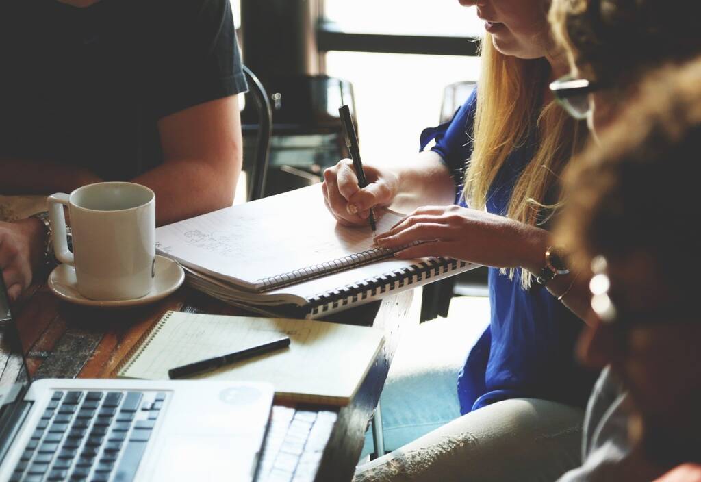 Group of adults meeting around a table, taking notes and having a laptop and coffee on the table.