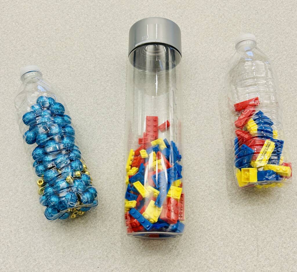 Three clear bottles with Legos in two and blue metal bells in the other