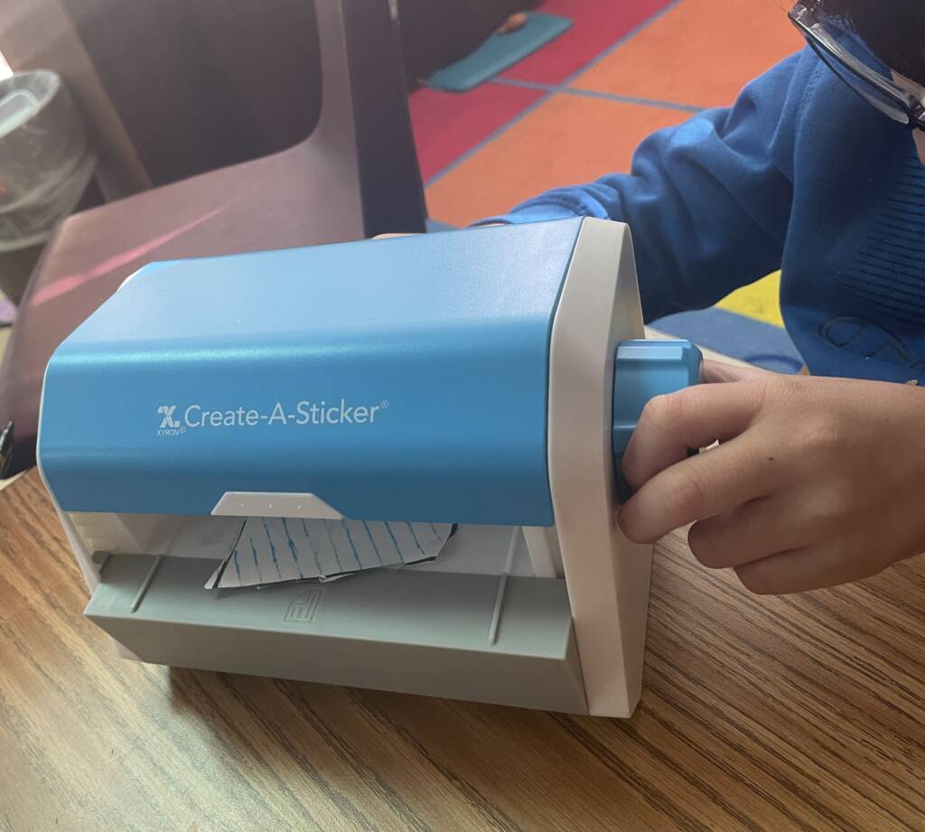 Student making the kite into a sticker with the Xyron machine.
