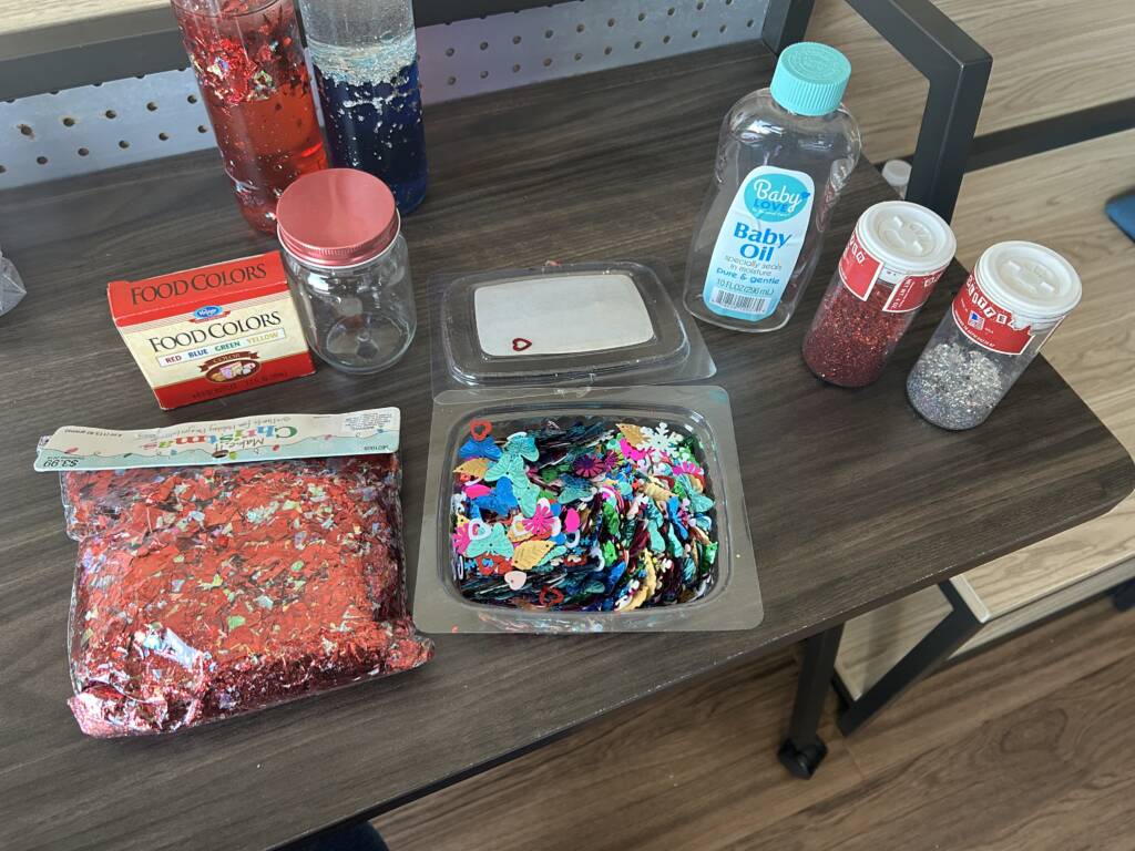 Materials to make the liquid sensory bottles that include confetti shapes, glitter, food coloring, and baby oil.