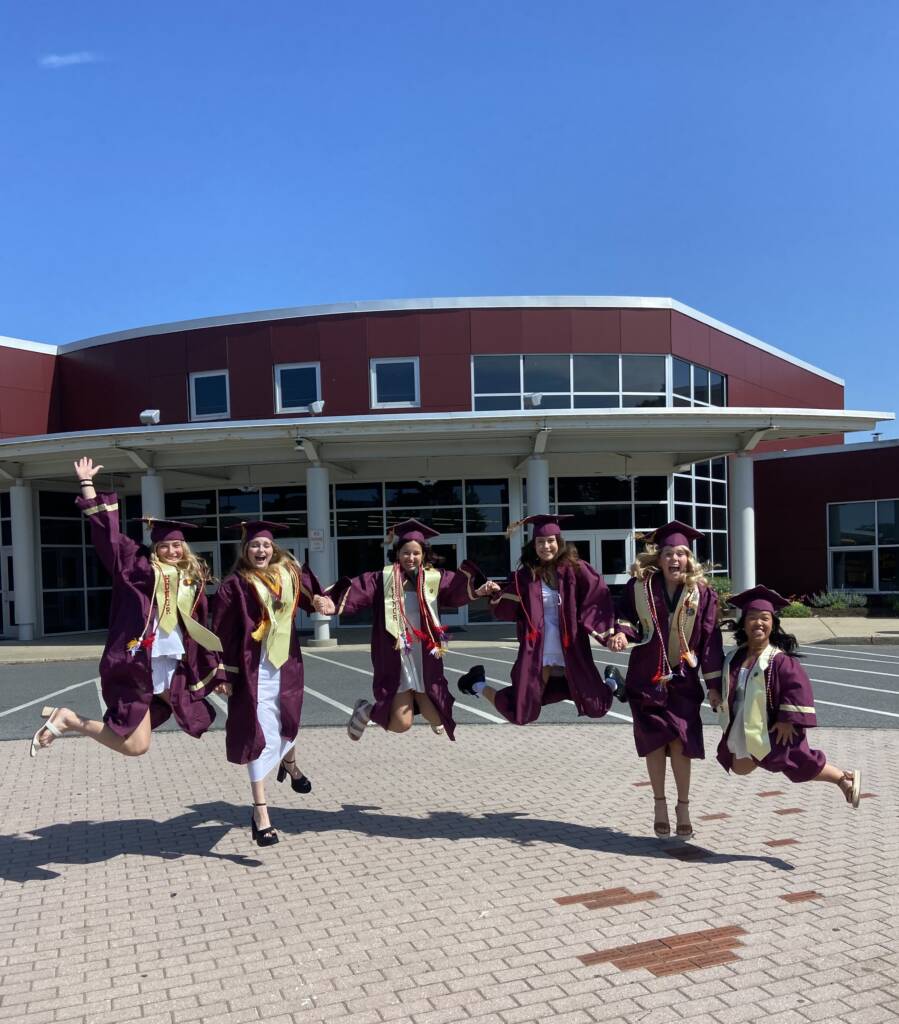 Six students in cap and gowns jumping in the air.