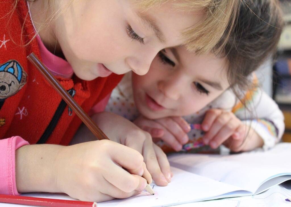 Two little girls working closely together on a book.