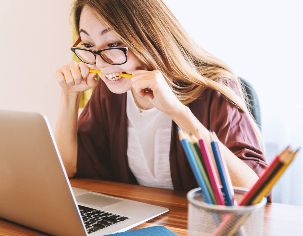 Woman looking at her laptop concerned and biting down on a pencil