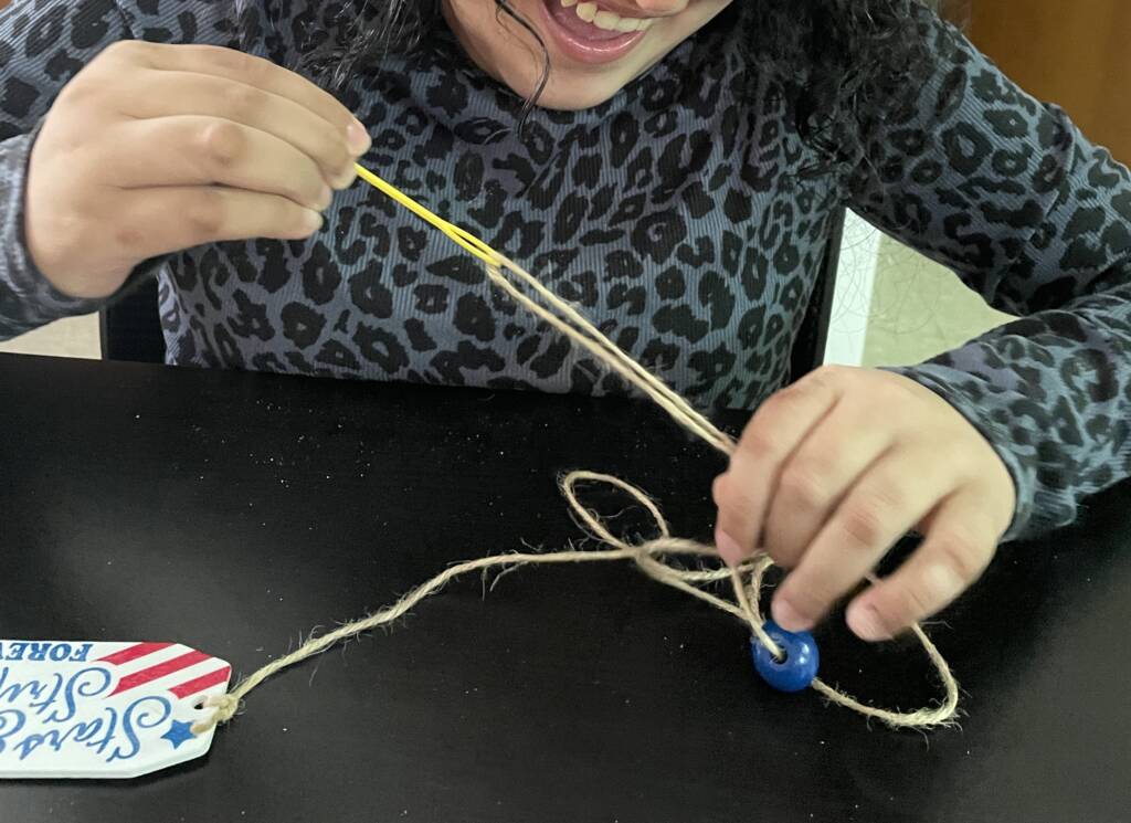 Student beading beads onto a string.