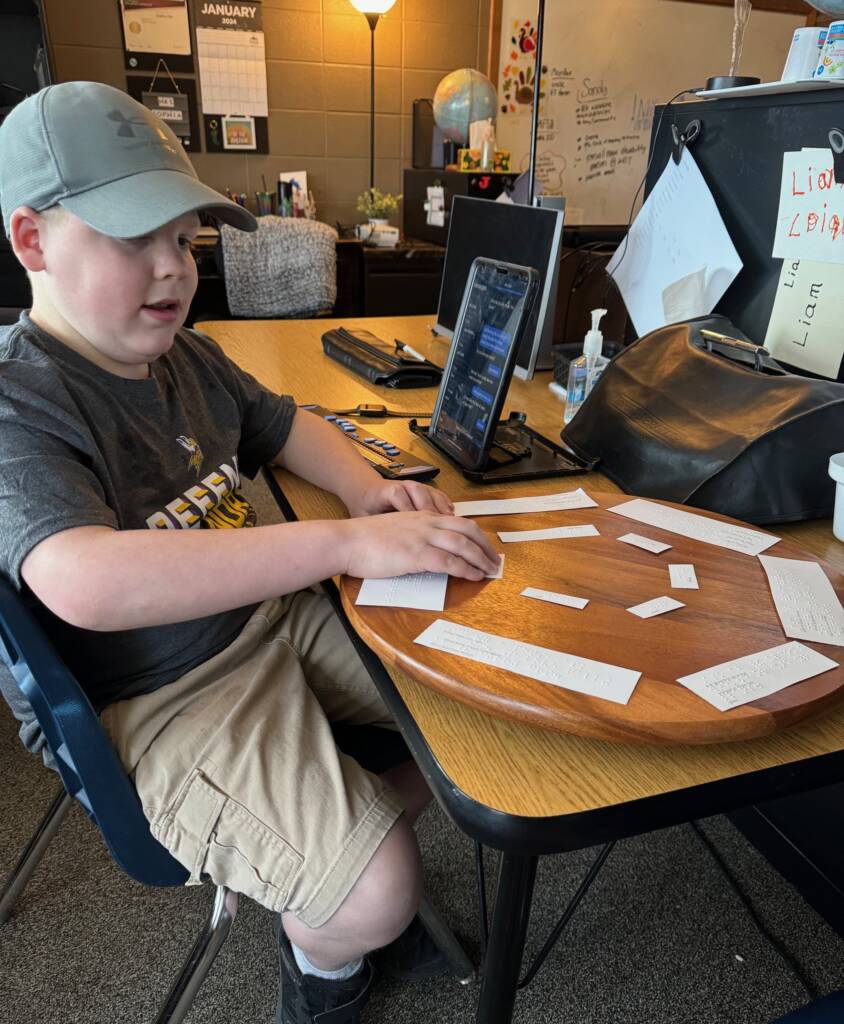 Liam reading his braille on the lazy Susan with his technology next to him to read the text messages.