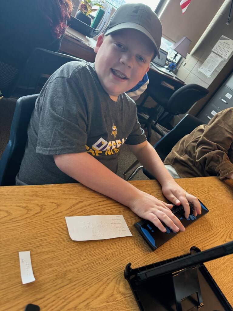 Liam with a smile as he reads his refreshable braille while doing this activity.
