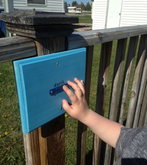 A child reading a sign in braille on their outdoor playground. The sign reads "north" in both print and braille.
