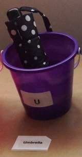 Bucket with umbrella inside; letter "u" in print and braille; word card "umbrella" in print and braille