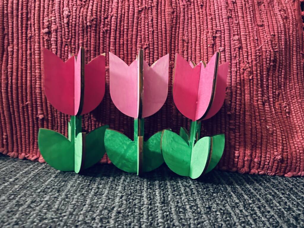 Three painted wooden tulips completed with red and a green stems. 