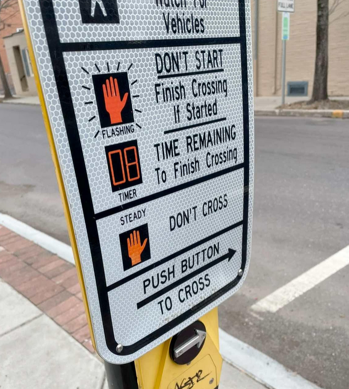 Crossing sign at a street corned to push the button for safe crossing.