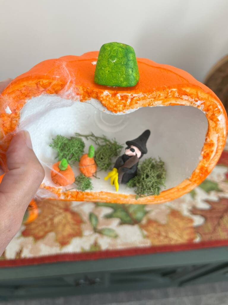 A foam pumpkin cut in half and a clay with can pumpkins in it made by a young student.